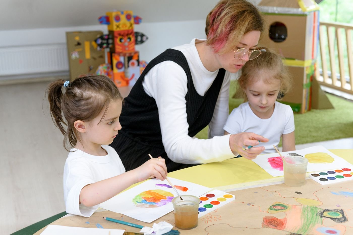 Erzieherin malt mit zwei Kindern mit Wasserfarben
