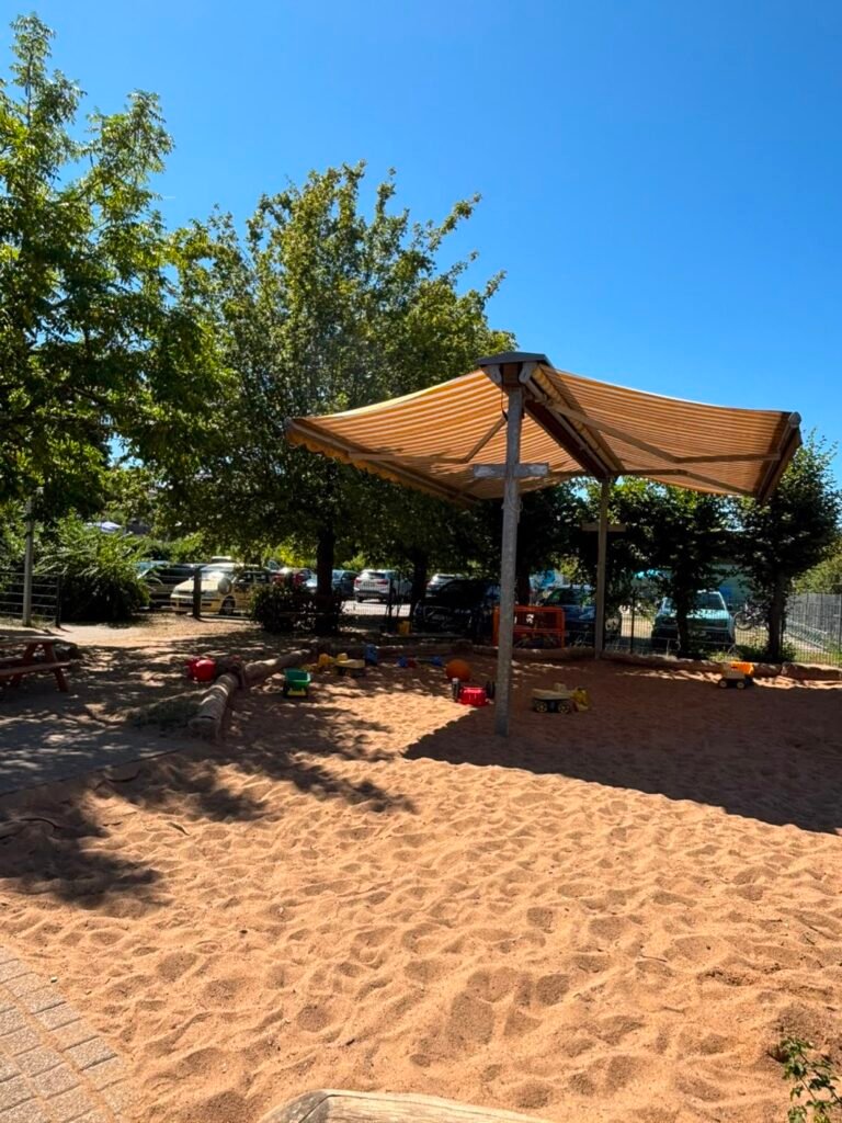 Großer Sandkasten mit Sonnensegel im Garten des Kindergartens